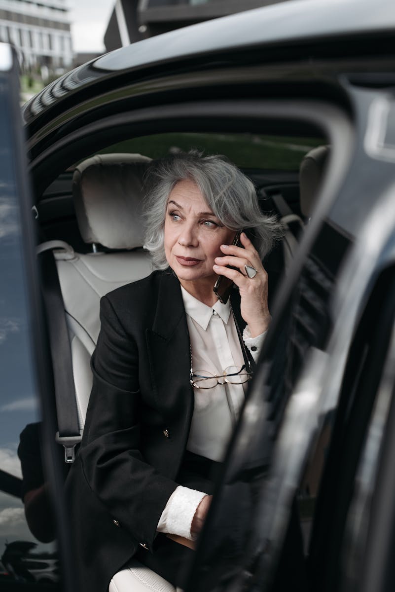 Elegant senior woman with grey hair talking on phone inside a car.